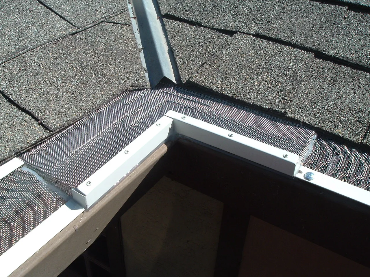 High-Flow Inside Miter installed at a white gutter corner beneath a shingle roof valley, with gutter guards connected on both sides